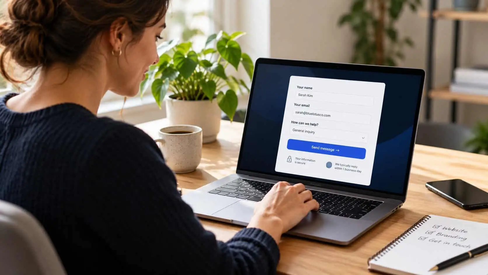 A small business owner at her laptop filling in a short contact form with name, email and a how can we help dropdown, a Send message button and a note saying replies come within one business day